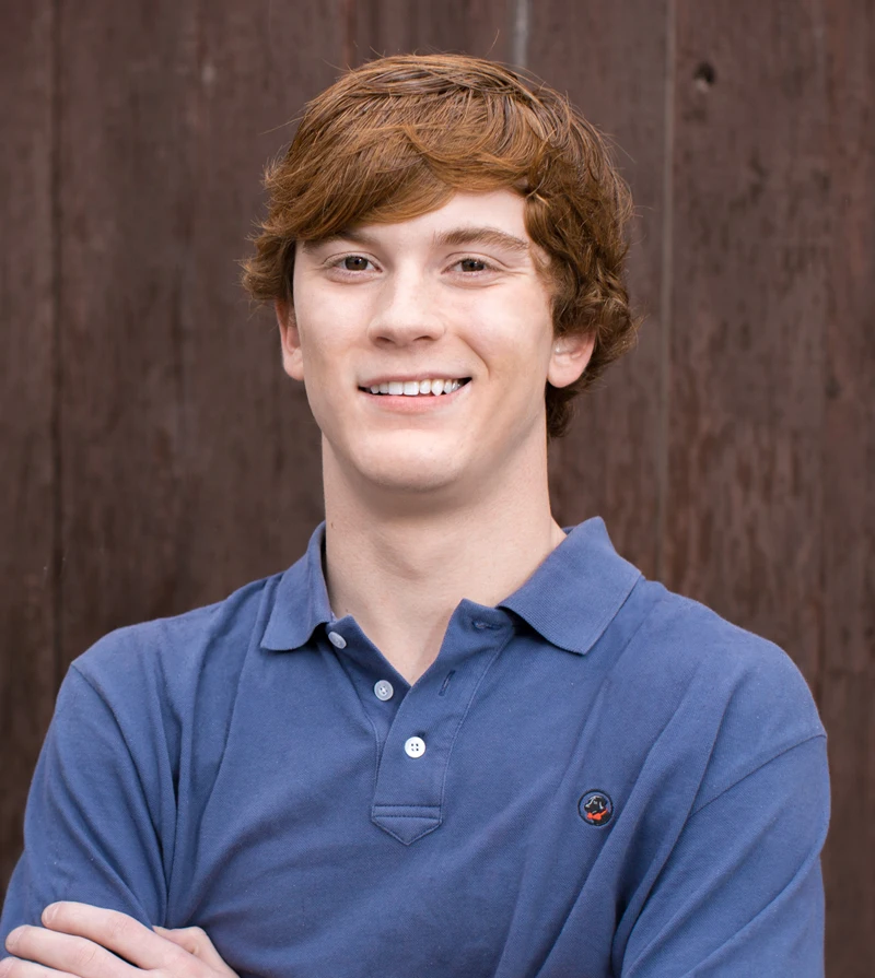 Dentist Northport AL Patient Showing Off Smile Young smiling teen in a blue polo shirt with red hairs with arms crossed posed in front of a wood backdrop