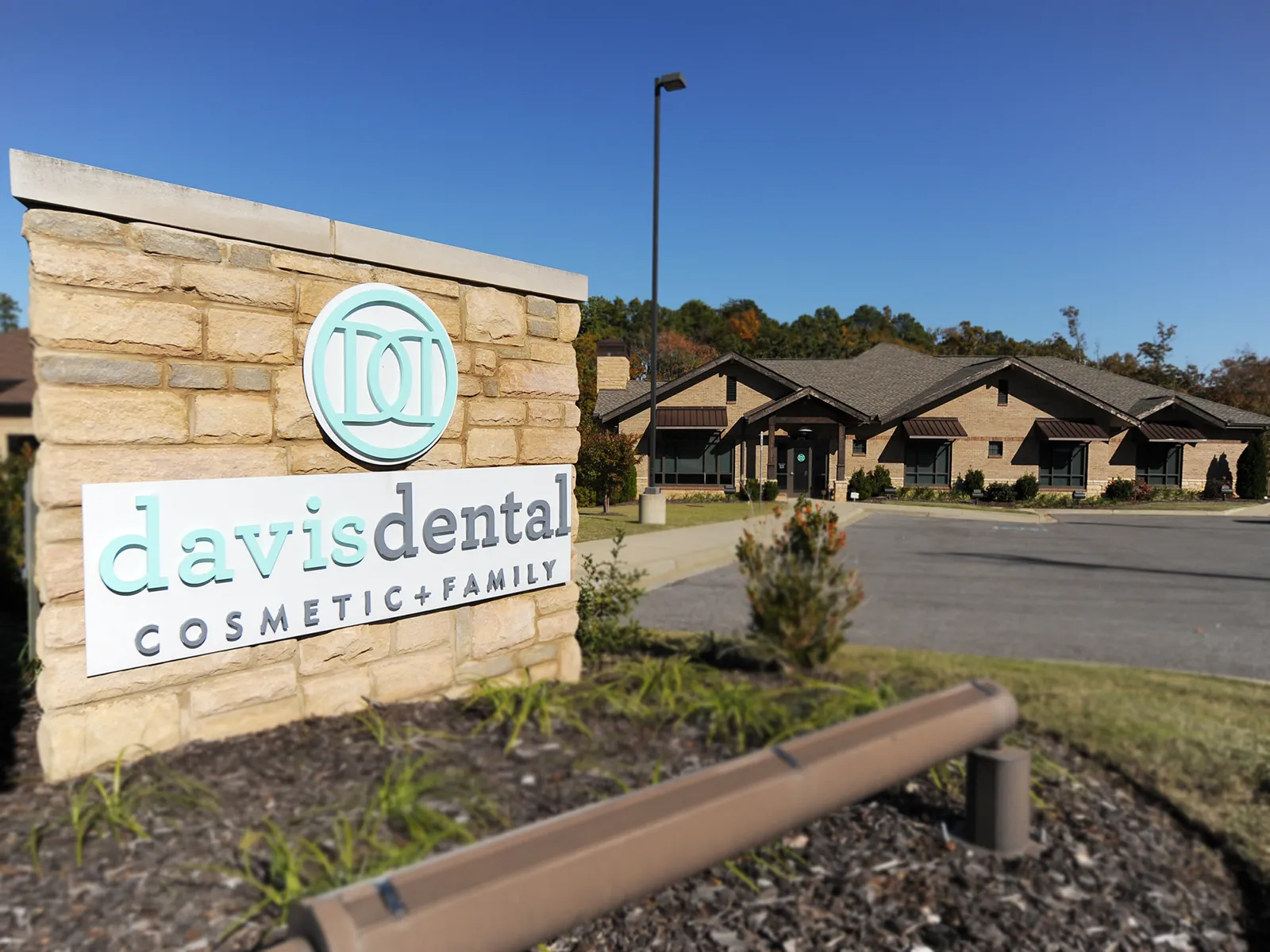 photograph of Davis Dental from the outside featuring the stone sign with clinic logo as well as the building